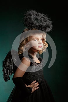 Children`s demon with black wings costume in carnival and religious style in the studio with an interesting emotion.