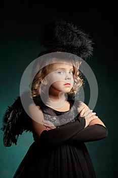 Children`s demon with black wings costume in carnival and religious style in the studio with an interesting emotion.