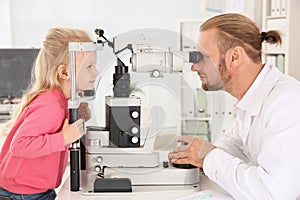 Children`s doctor examining little girl with ophthalmic equipment photo