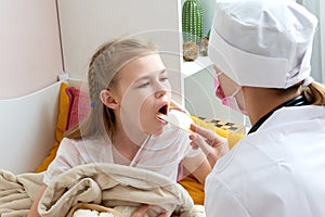 Children`s doctor examining little girl`s throat at home with a tongue depressor