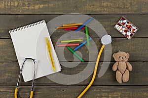Children& x27;s doctor or pediatrician concept - blank notepad, pills, yellow stethoscope, Teddy bear toy, crayons