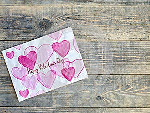 Children`s drawing with hearts and an inscription for Valentine`s day, lying on wooden textured boards of light gray color