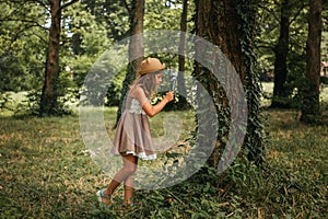 Children& x27;s education and curiosity. Caucasian little girl in a straw hat and dress looks at the tree bark through a