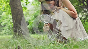 Children's education and curiosity. Cute little girl in a straw hat looks at the grass through a magnifying glass