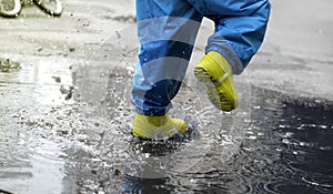 Children& x27;s feet close-up in rubber boots and non-wet pants. A child jumps in a puddle creating splashes