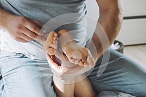 Children`s feet in hands of father. Dad tickles feet of kid sitting on them. Family, having fun at home