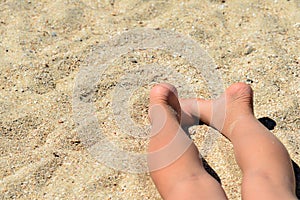 Children`s feet lie on the sea sand, the child sunbathes on a sunny beach