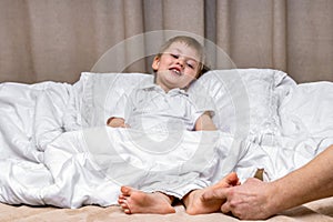 Children's feet under a blanket are tickled by dad's hand