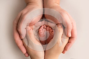 Children& x27;s foot in the hands of mother, father, parents. Feet of a tiny newborn close up. Little baby legs.