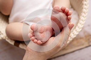 Children& x27;s foot in the hands of mother, father, parents. Feet of a tiny newborn close up. Little baby legs.