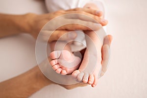 Children& x27;s foot in the hands of mother, father, parents. Feet of a tiny newborn close up. Little baby legs.