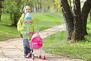 Children`s friendship. Small friends. Children walk in green park. Little boy and girl with toy carriage for doll