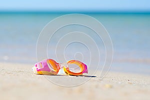 Children`s goggles for scuba diving lie on the sandy beach against the background of the sea.