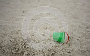 Children`s green bucket lies on the sea coast. The bucket is lying on the sand. Space for text. Vacation on the ocean coast.