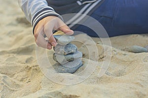 Children`s hand builds a tower of stones on the yellow sand1