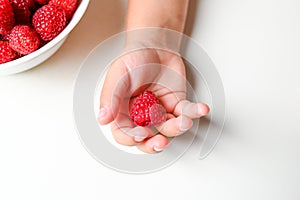 Children& x27;s hand hold a handful of raspberry on a white background Close Up