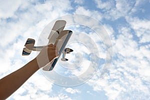 Children`s hand holds a toy plane against the sky,blue sky white clouds