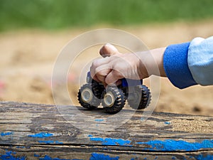 Children`s hand holds a toy. From under the fingers, only the wheels of the car are visible.