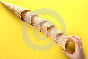 Children`s hand pulls one empty waffle cup for ice cream. Waffle cups lie diagonally on a yellow background and a children`s han