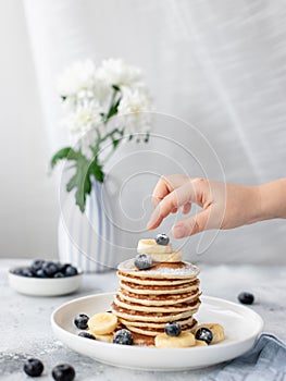 Children`s hand reaches for a stack of pancakes with berries. delicious homemade breakfast.