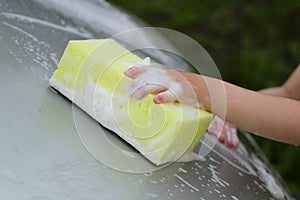 Children`s hand with a yellow sponge with foam washes the car