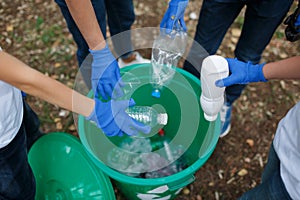 Children`s hands in blue latex gloves holding plastic bottles on a park ground background. Ecology protection concept.
