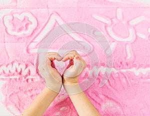 Children`s hands depict the heart on the background of decorative sand.