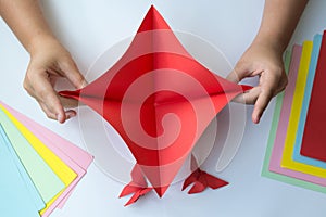 Children`s hands do origami butterfly from colored paper on white background.