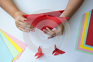 Children`s hands do origami butterfly from colored paper on white background.