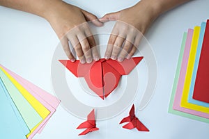 Children`s hands do origami butterfly from colored paper on white background.