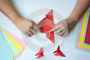 Children`s hands do origami butterfly from colored paper on white background.