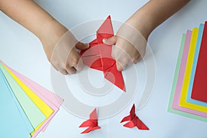 Children`s hands do origami butterfly from colored paper on white background.