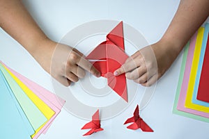 Children`s hands do origami butterfly from colored paper on white background.