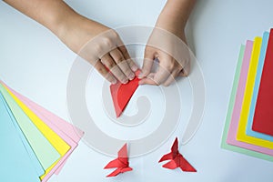 Children`s hands do origami butterfly from colored paper on white background.