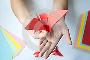 Children`s hands do origami butterfly from colored paper on white background.