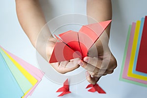 Children`s hands do origami butterfly from colored paper on white background.