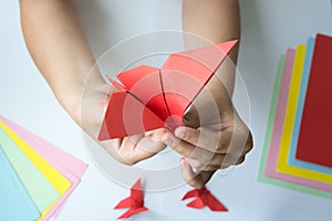 Children`s hands do origami butterfly from colored paper on white background.