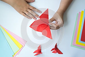 Children`s hands do origami butterfly from colored paper on white background.