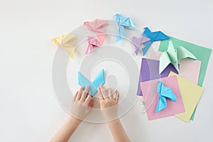 Children`s hands do origami from colored paper on white background. lesson of origami