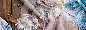 Children`s hands and dough with flour on a wooden table and a green towel, rolling pin and board.