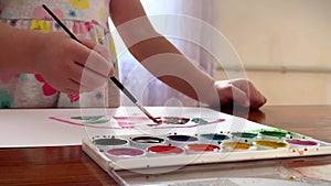 Children's hands draw with watercolors on a sheet, close-up view