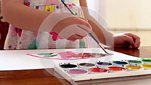 Children's hands draw with watercolours on a sheet, close-up view