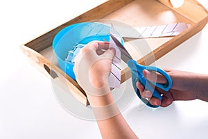 Children`s hands hold blue scissors and cut the paper. On a wooden tray are Montessori materials for a lesson