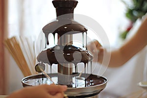 Children`s hands hold fruit on a stick in a chocolate fountain