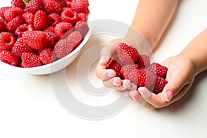 Children& x27;s hands hold a handful of raspberry on a white background. Bowl with ripe juicy raspberries. Healthy eating