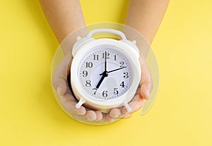 Children& x27;s hands hold a white alarm clock . Yellow background. Concept of time. Copy spase