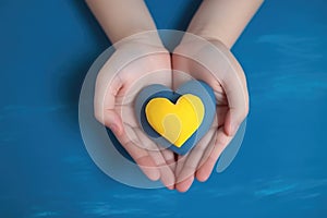 Children\'s hands hold a yellow and blue heart. The concept of Ukrainian patriotism, love for Ukraine.