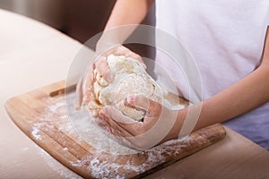 Children`s hands knead the dough on a wooden cutting board. close-up. dough recipe, cooking technology