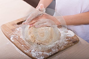 Children`s hands knead the dough on a wooden cutting board. close-up. dough recipe, cooking technology