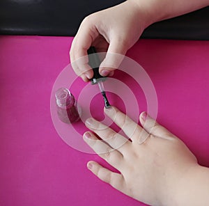 Children`s hands paint their nails with pink shiny nail polish.